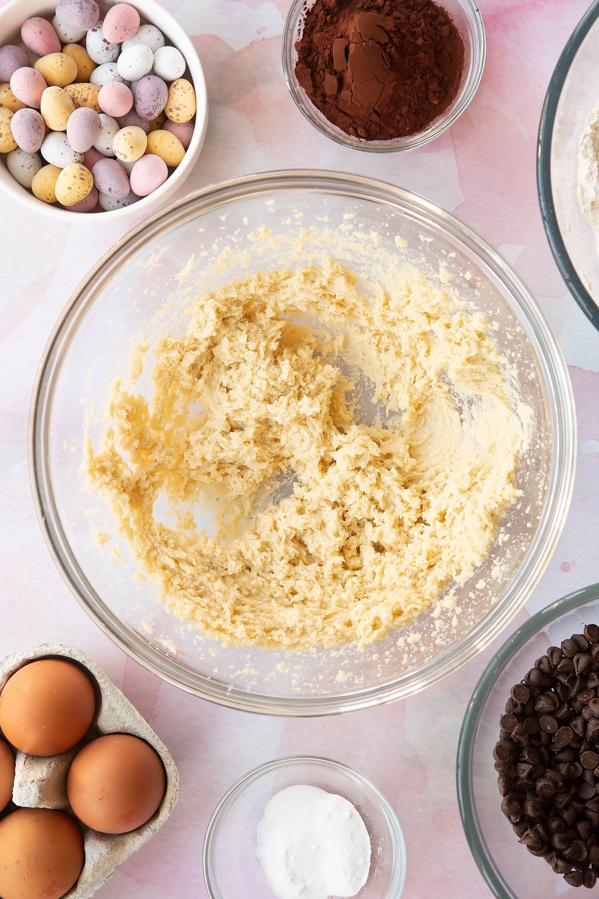 Butter and golden granulated sugar beaten together in a bowl. Ingredients to make Chocolate Easter cookies surround the bowl.