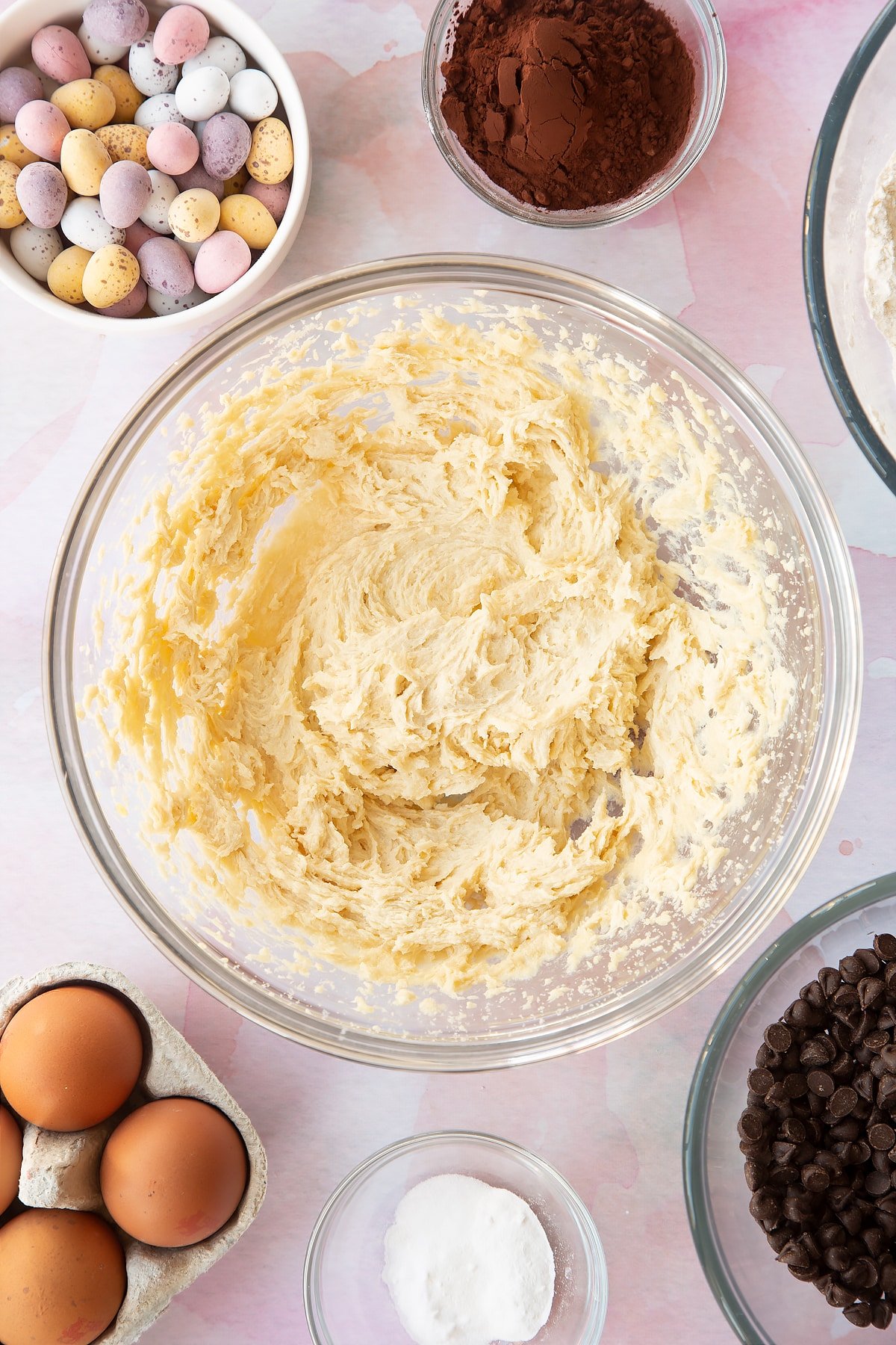 Butter, golden granulated sugar and egg beaten together in a bowl. Ingredients to make Chocolate Easter cookies surround the bowl.