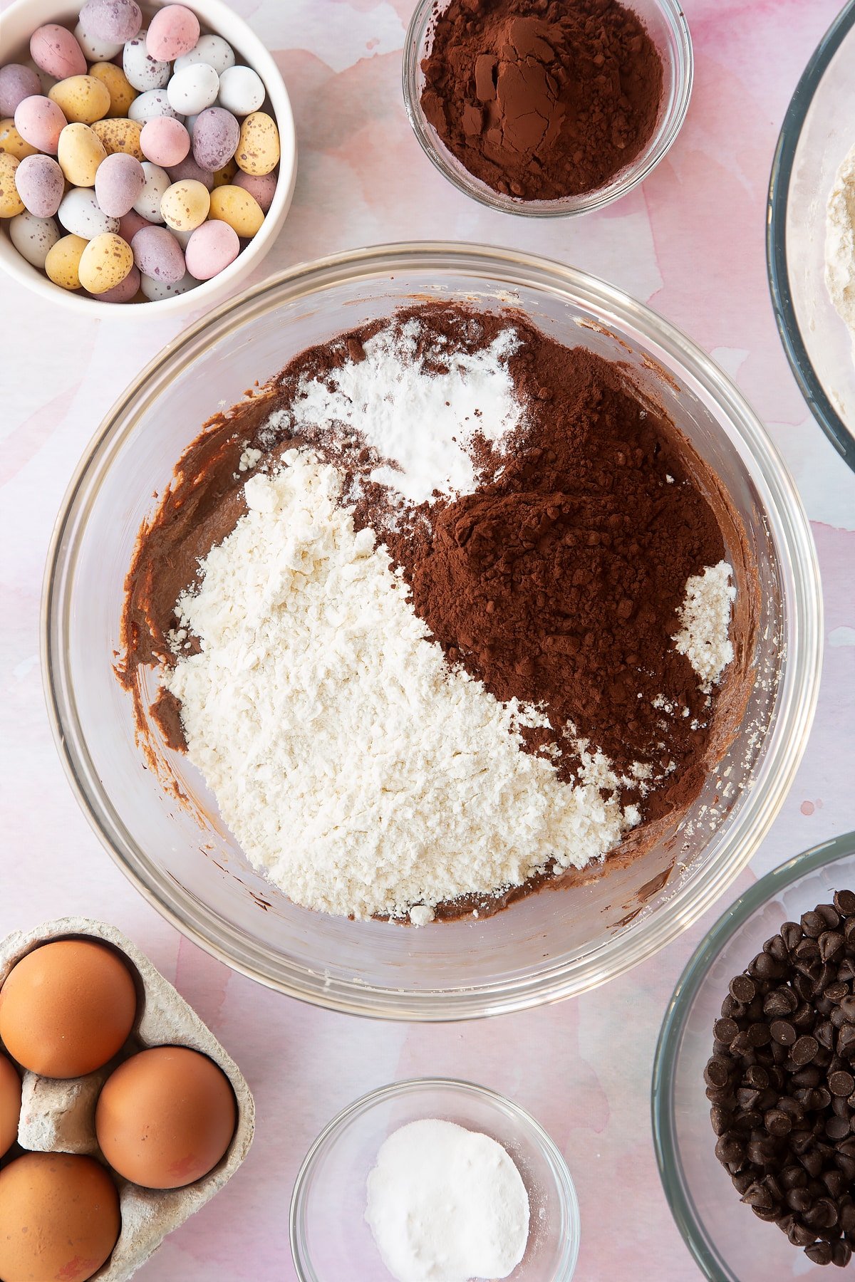 Butter, sugar, egg and dark chocolate beaten together in a bowl with flour and cocoa on top. Ingredients to make Chocolate Easter cookies surround the bowl.