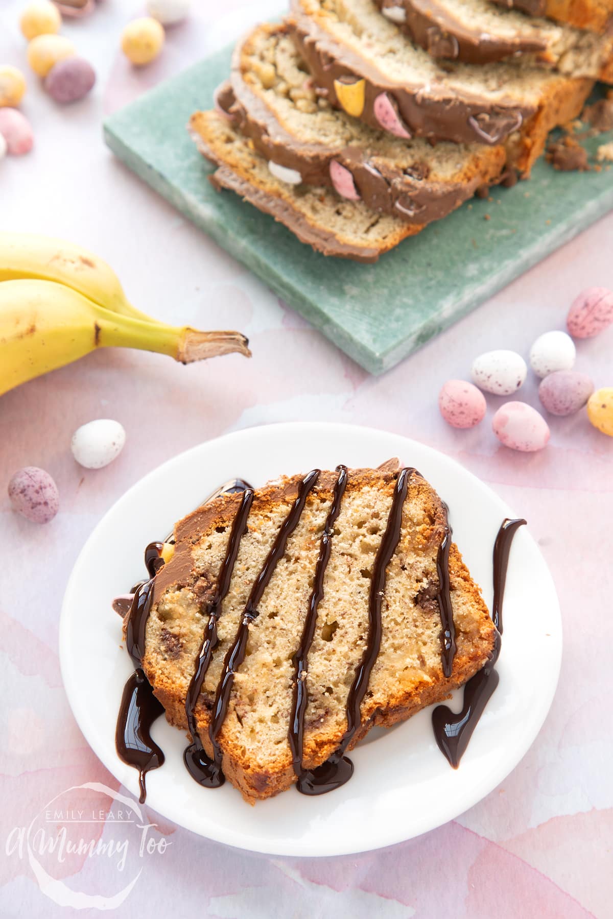 A slice of Easter banana bread on a white plate. The slice is drizzled with chocolate sauce.