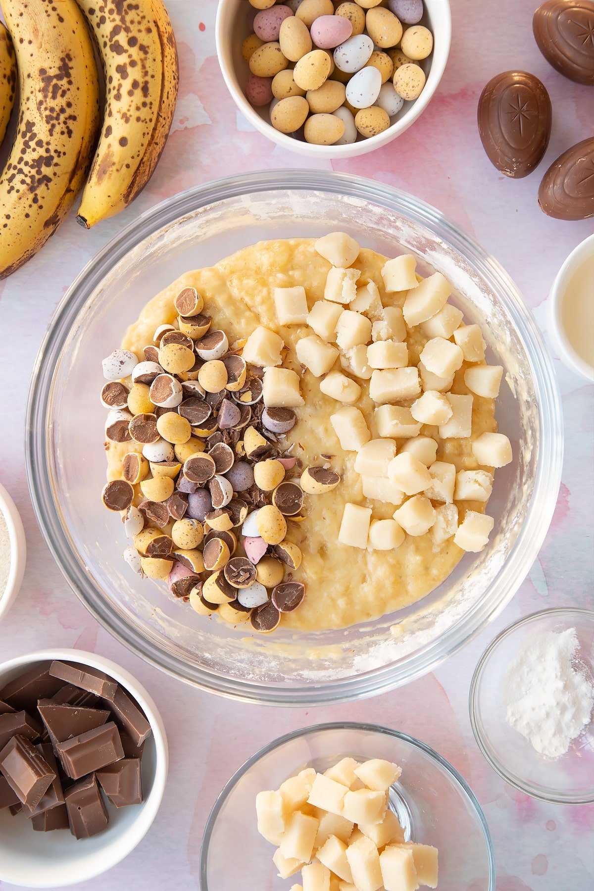 Banana bread batter in a mixing bowl, topped with chopped Mini Eggs and pieces of marzipan.