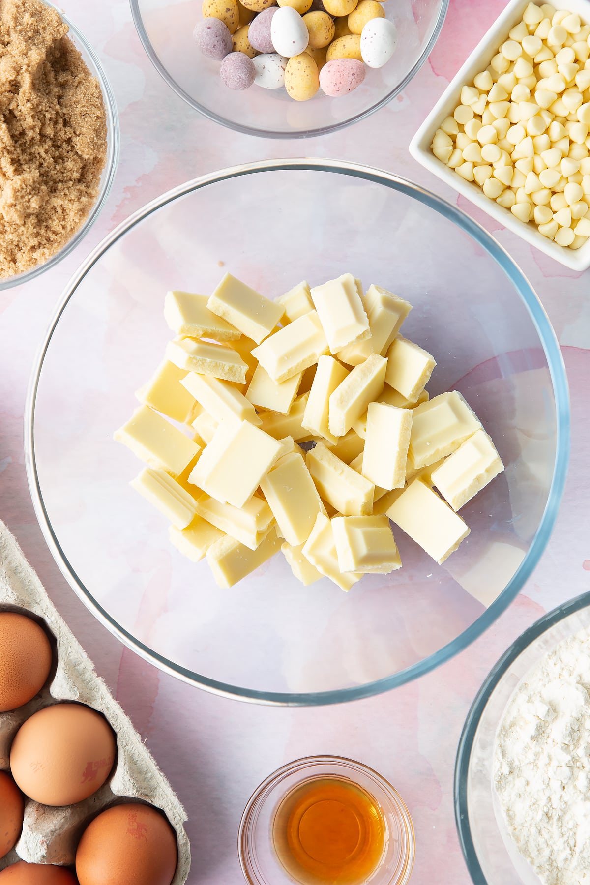 White chocolate chunks in a bowl. Ingredients to make Mini Egg blondies surround the bowl. 