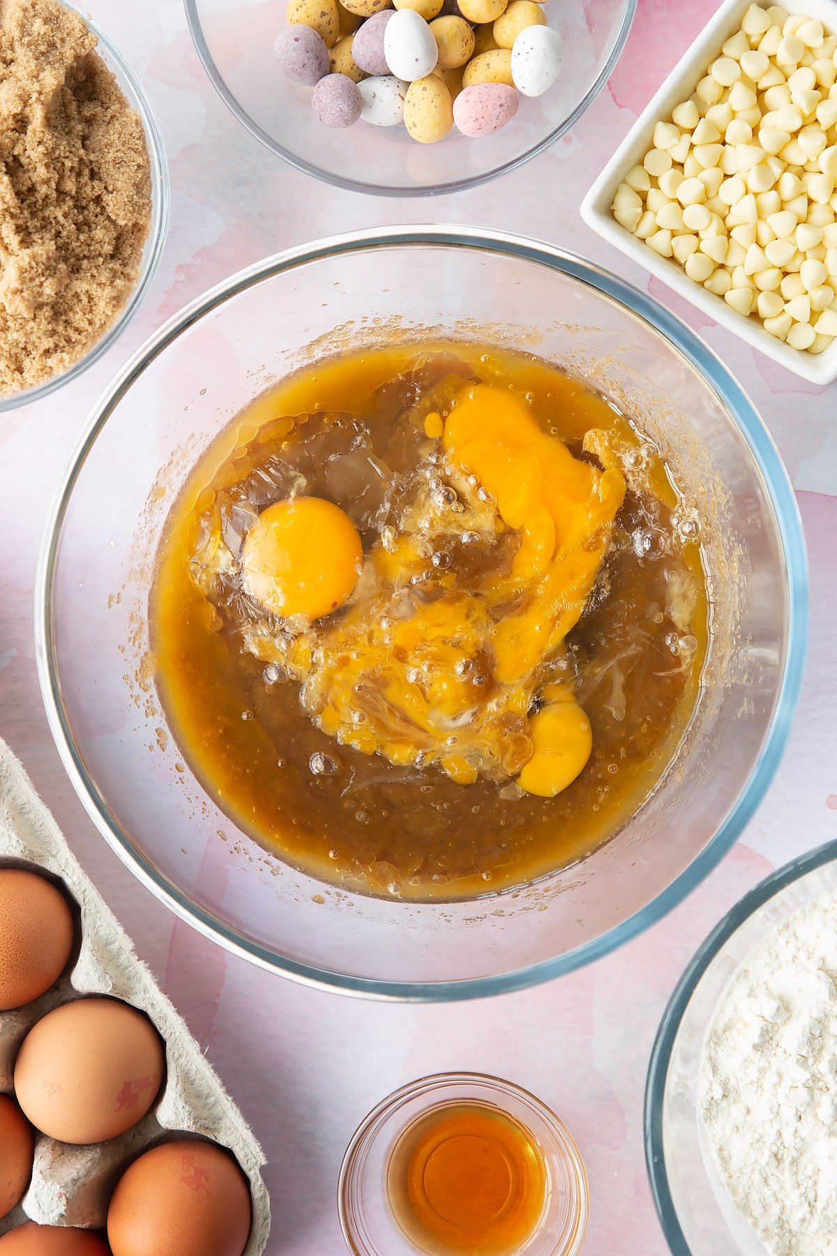 Melted butter and sugar mixed together in a bowl with eggs on top. Ingredients to make Mini Egg blondies surround the bowl. 