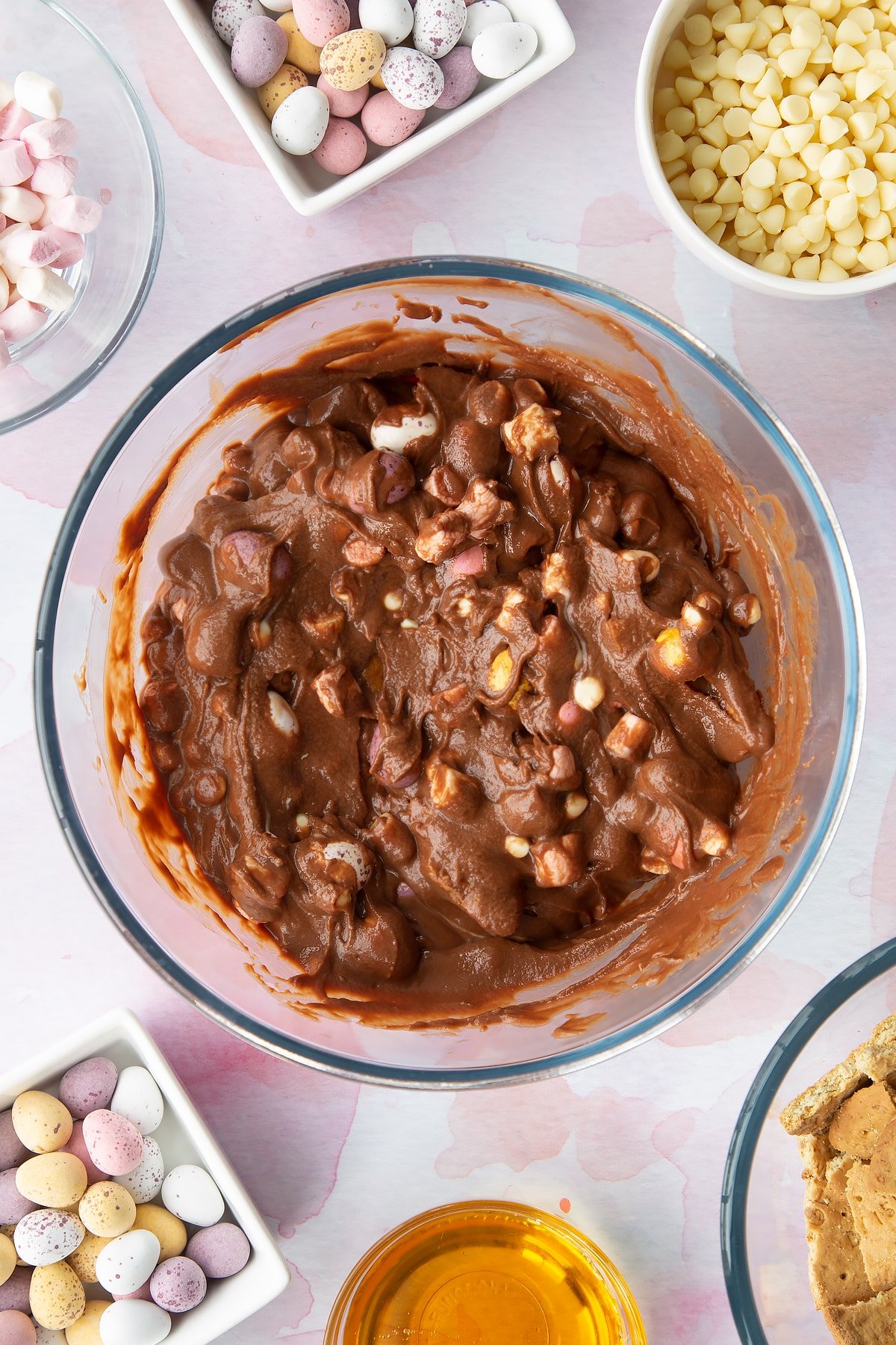 Rocky road mix in a glass mixing bowl. Ingredients to make Mini Egg rocky road surrounds the bowl.