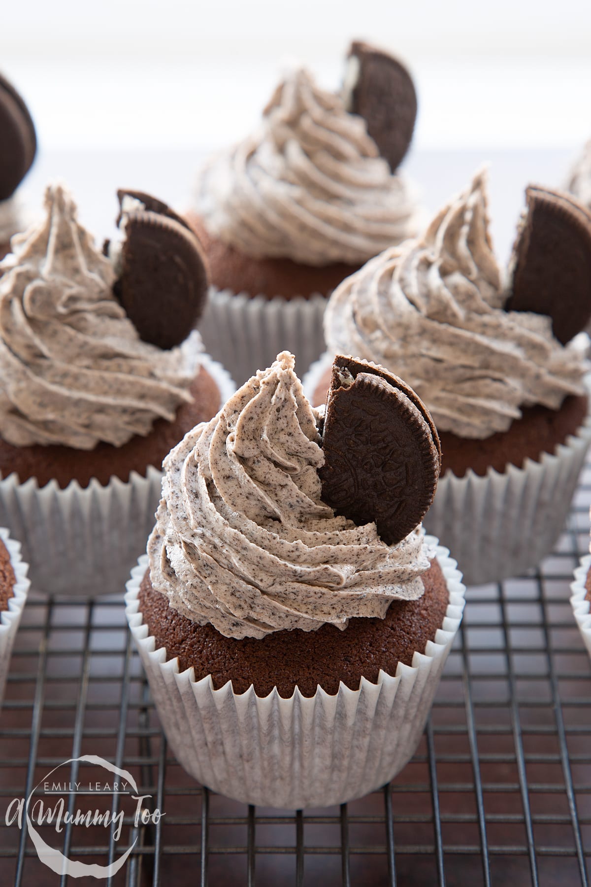 Front view shot of chocolate cupcake topped with oreo buttercream and half an oreo on a wire rack