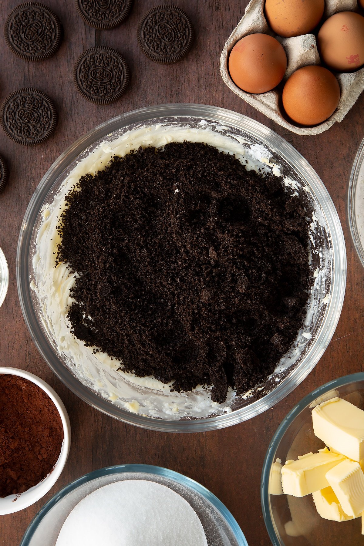 Overhead shot of buttercream mix topped with oreo crumbs in a large clear bowl