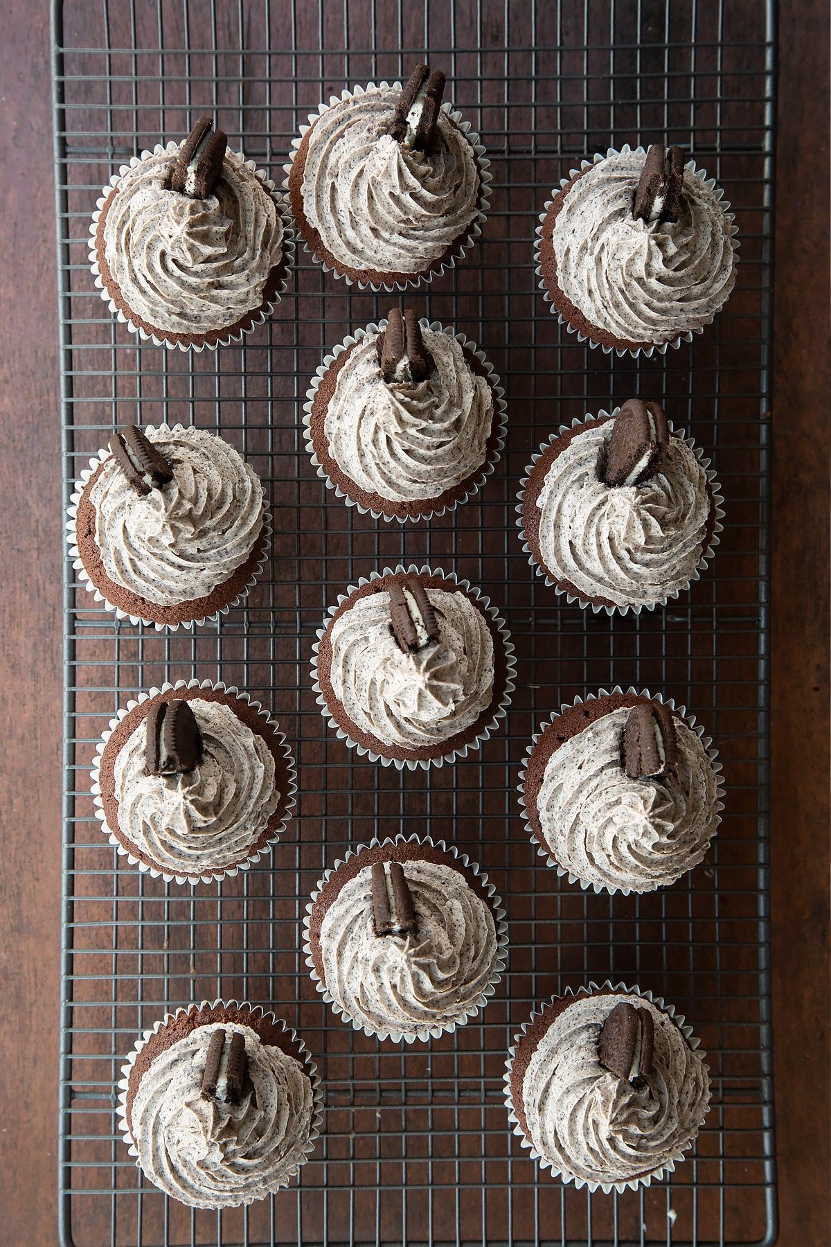 Overhead shot of oreo butter cream topped chocolate cupcakes with half an oreo in the side on a wire rack