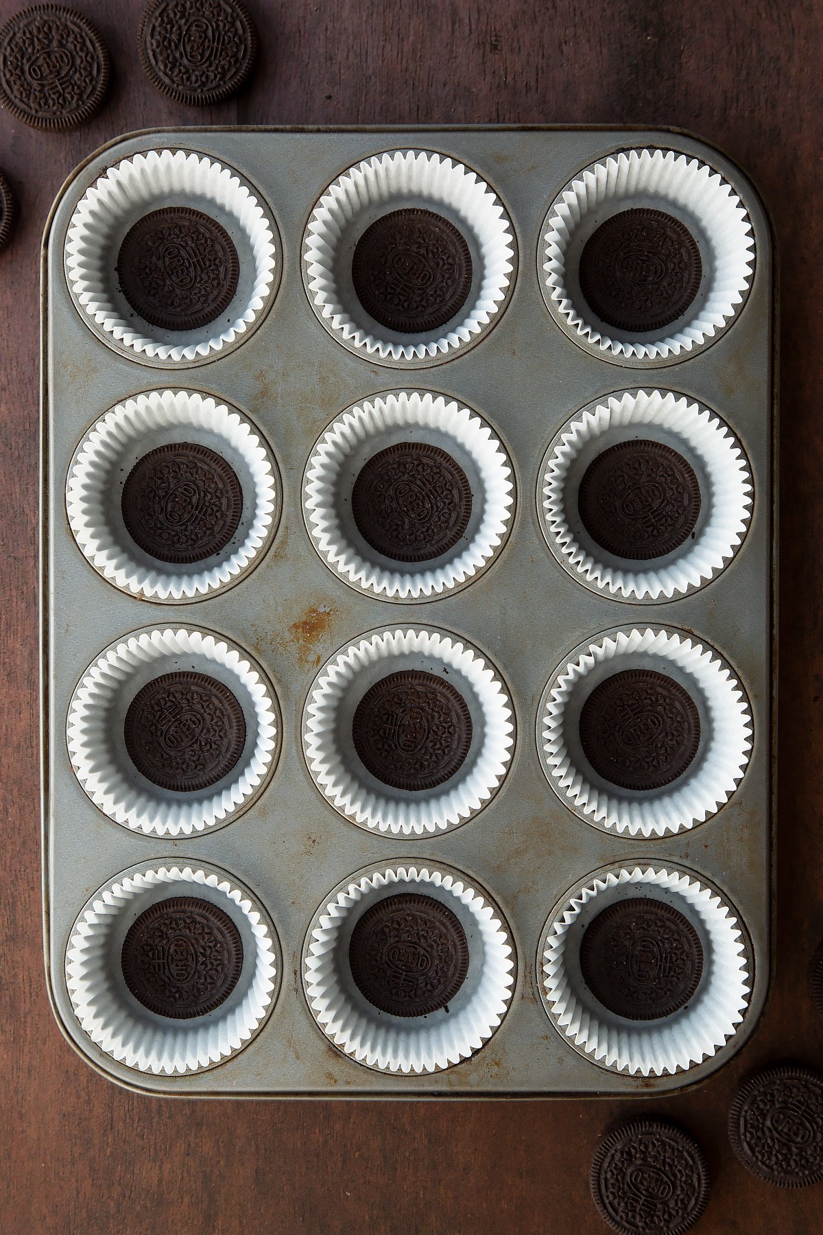 Overhead shot of 12 cupcake liners in a cupcake tray with oreos at the bottom of each one