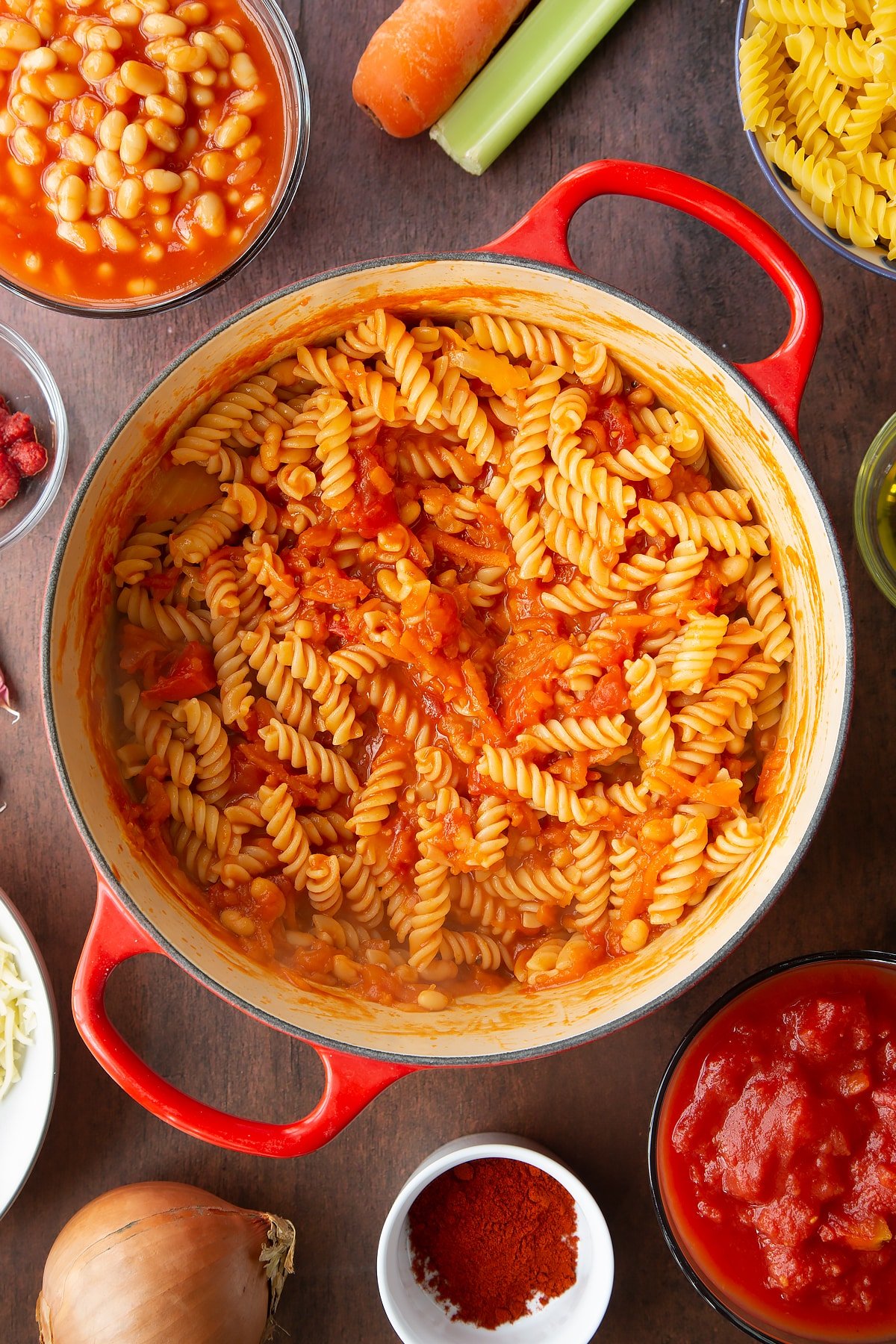 Baked beans and pasta in a saucepan. Ingredients to make pasta and baked beans surround the pan.