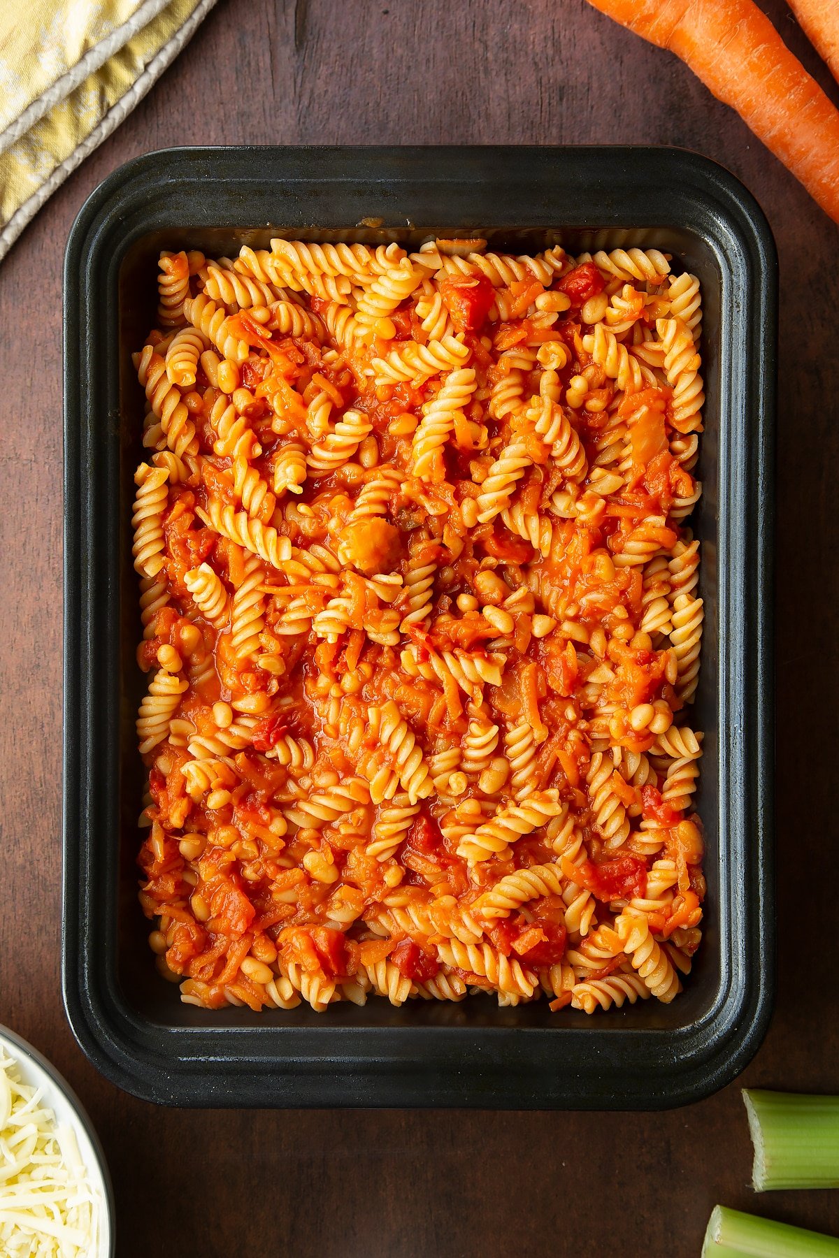 Baked beans and pasta in a tray. Ingredients to make pasta and baked beans surround the tray.