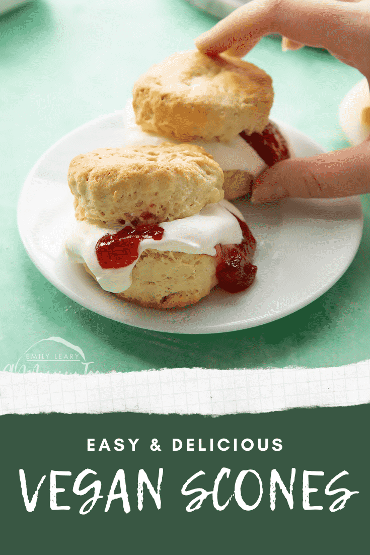 Two dairy free scones on a white plate. They are filled with jam and vegan whipped cream. A hand reaches for one. Caption reads: easy & delicious dairy free scones