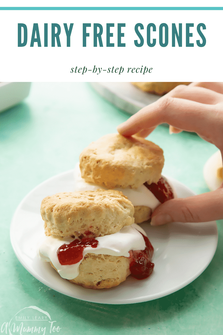 Two dairy free scones on a white plate. They are filled with jam and vegan whipped cream. A hand reaches for one. Caption reads: dairy free scones step-by-step recipe