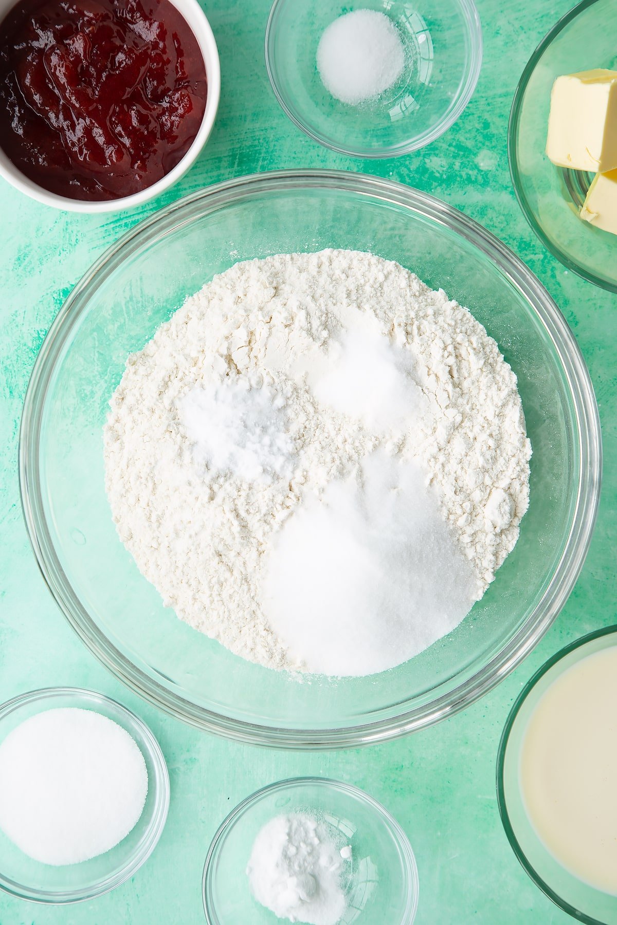 Flour, sugar, salt and bicarbonate of soda in a bowl. Ingredients to make dairy free scones surround the bowl.