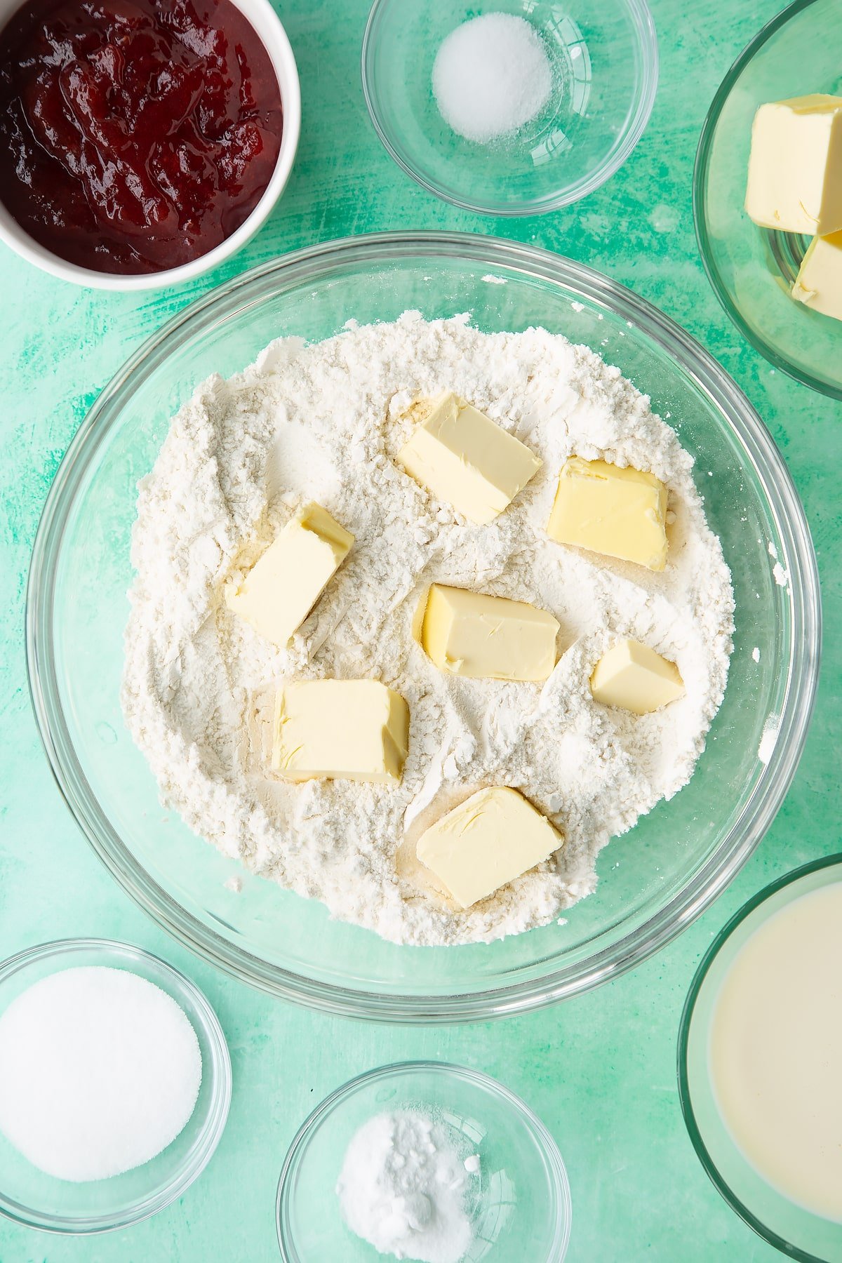 Flour, sugar, salt and bicarbonate of soda mixed together in a bowl with cubed vegan butter on top. Ingredients to make dairy free scones surround the bowl.