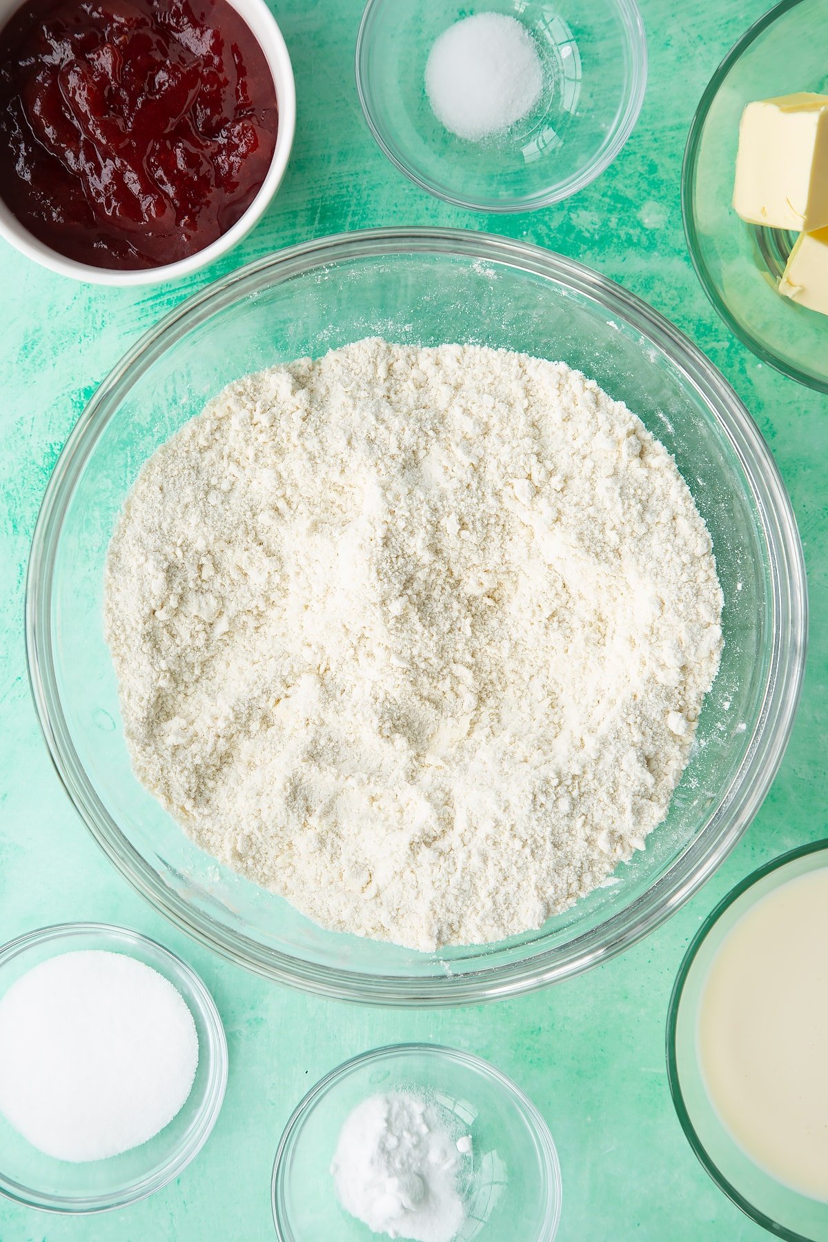 Flour, sugar, salt, bicarbonate of soda and vegan butter rubbed together in a bowl. Ingredients to make dairy free scones surround the bowl.