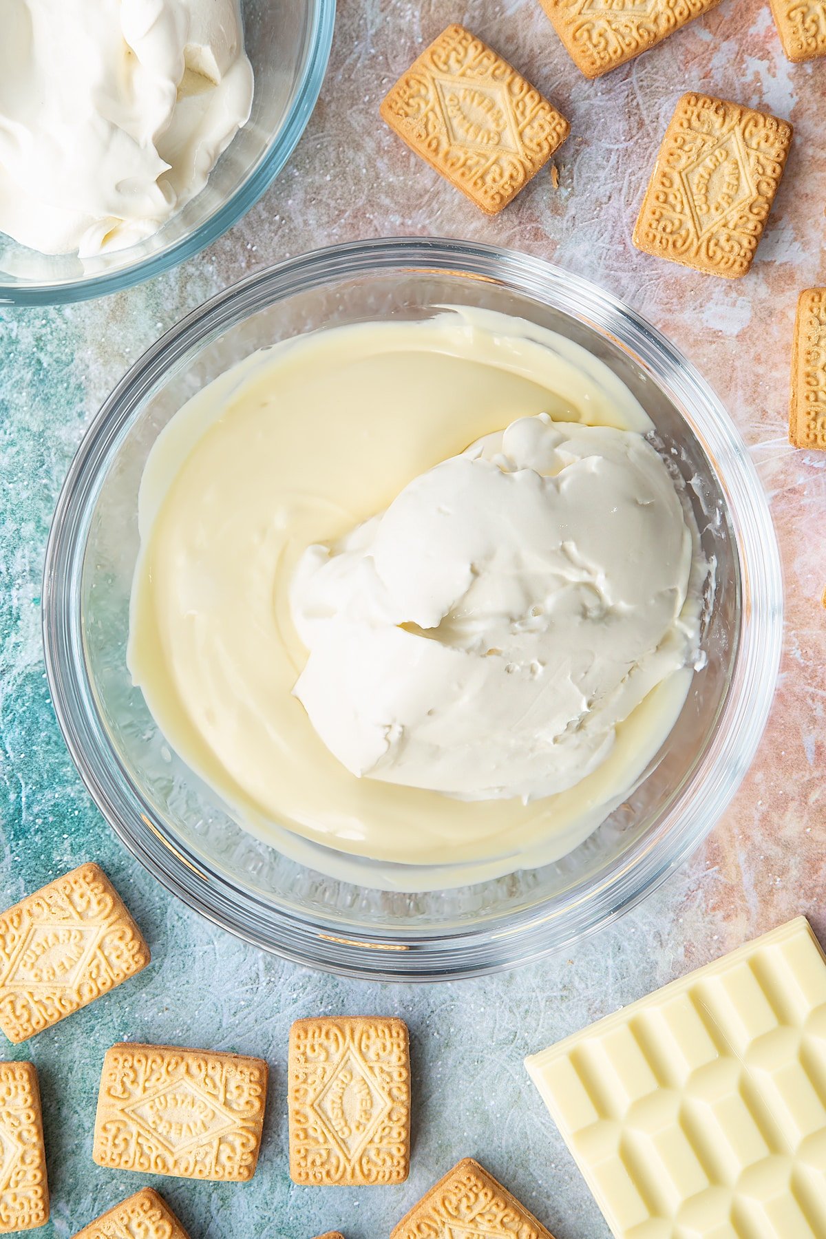 Overhead shot of melted white chocolate and cream cheese in a large clear bowl