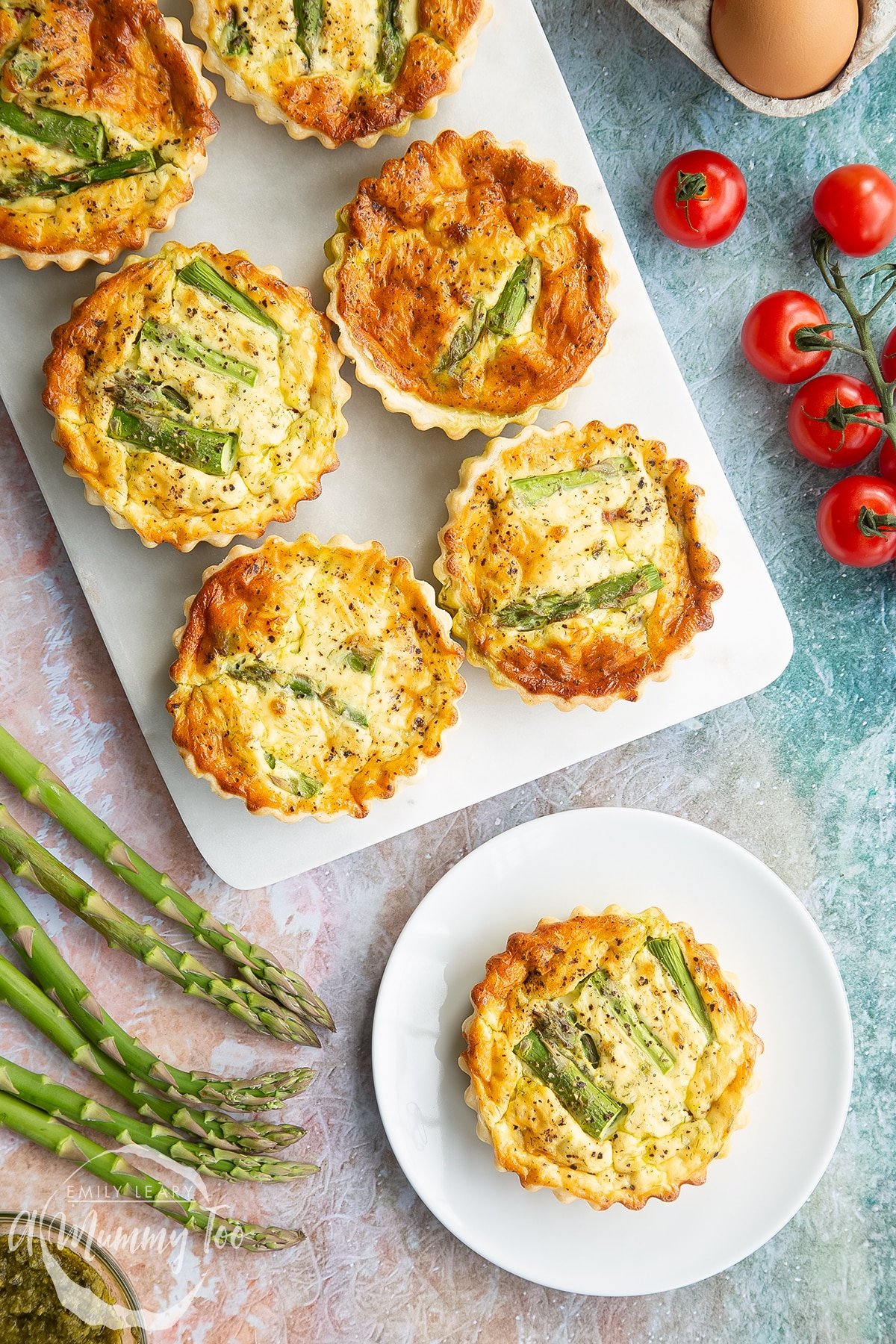 Asparagus tartlets on a white marble board. One is on a white plate. Shown from above. 