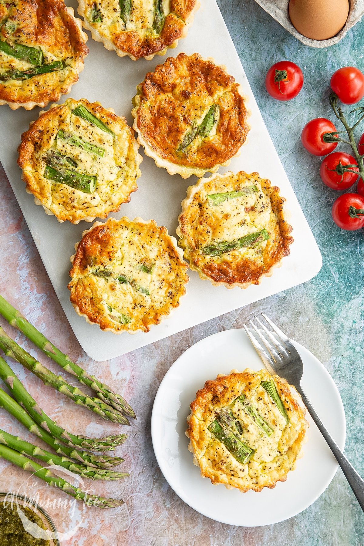 Asparagus tartlets on a white marble board. One is on a white plate with a fork. Shown from above. 