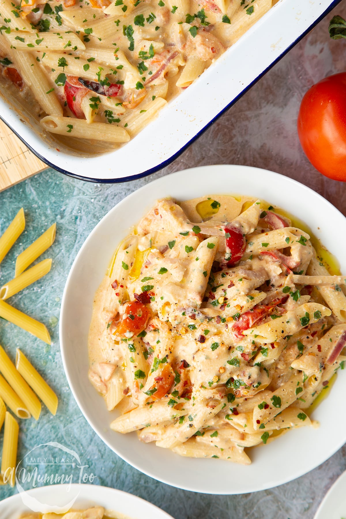 Close up of baked feta pasta in a white bowl, garnished with parsley and chilli flakes. 