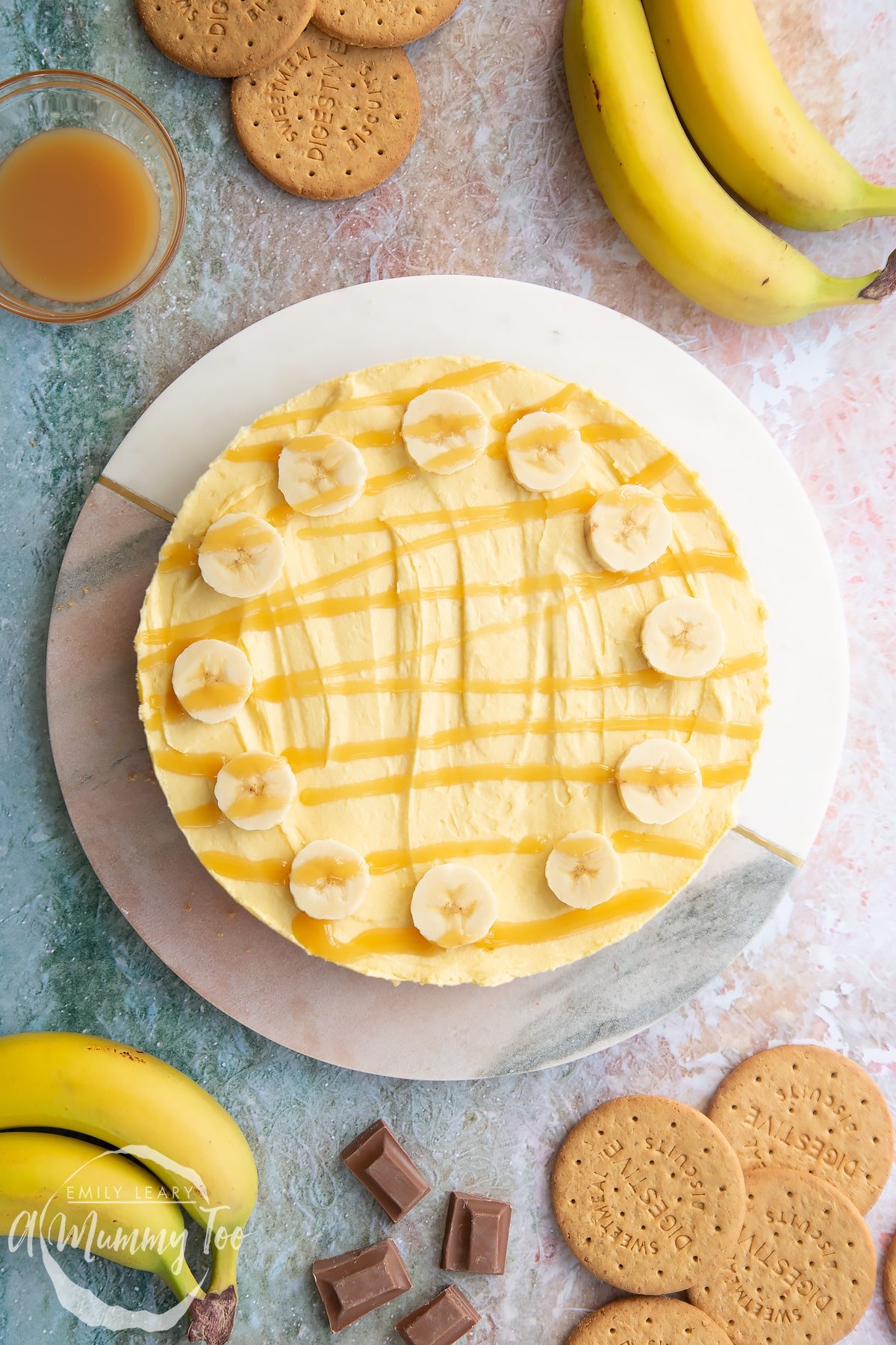 Banoffee pie cheesecake topped with banana slices and drizzled with toffee sauce on a white and pink marble board. 