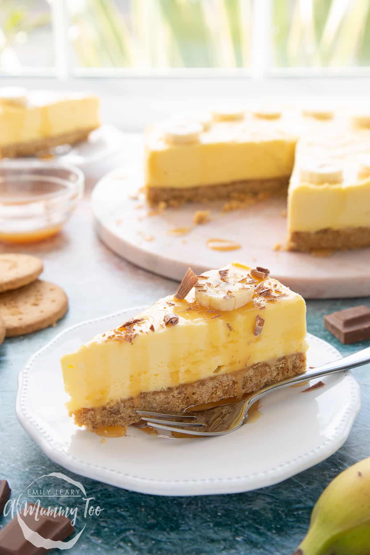 A slice of banoffee pie cheesecake on a white plate with a fork resting beside it.