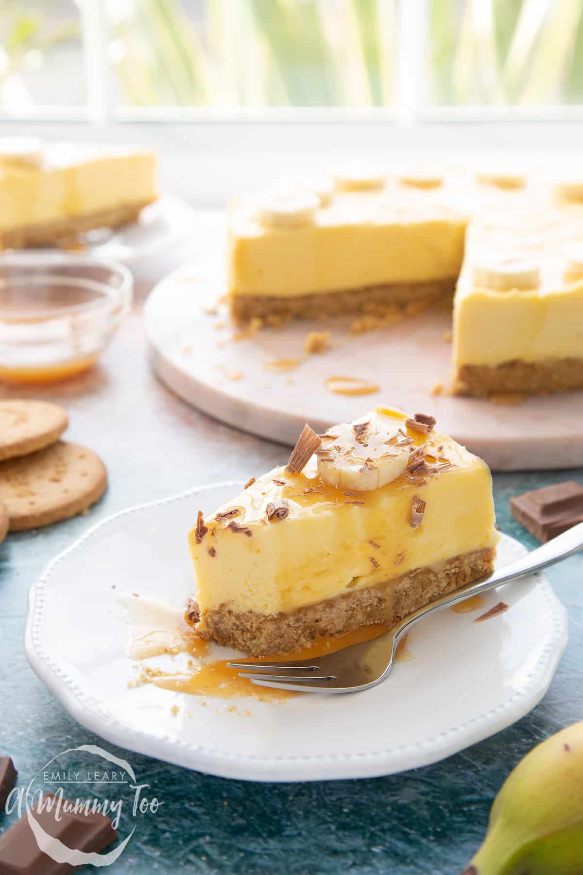 A slice of banoffee pie cheesecake on a white plate. A piece has been eaten and a fork rests beside it.