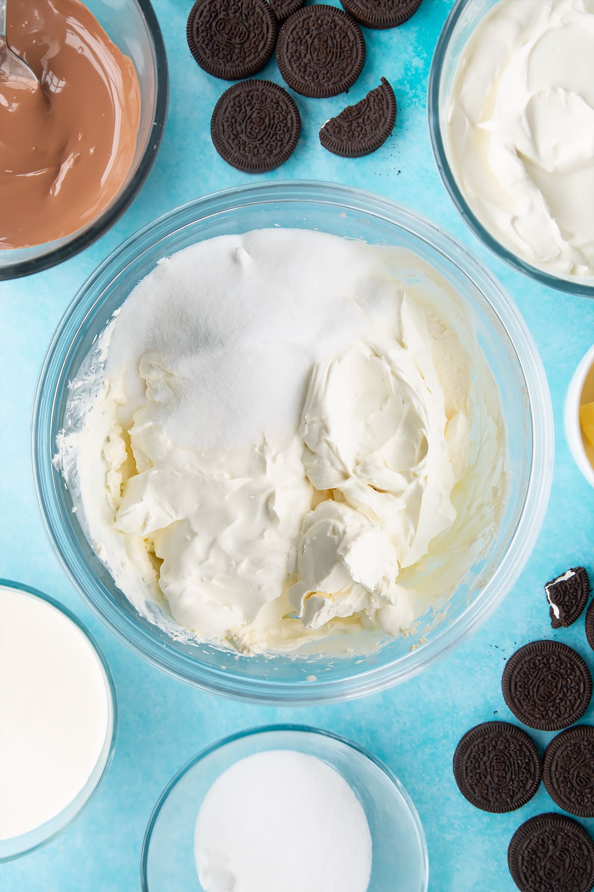 Overhead shot of whipped cream, cream, sugar and cream cheese in a large clear bowl