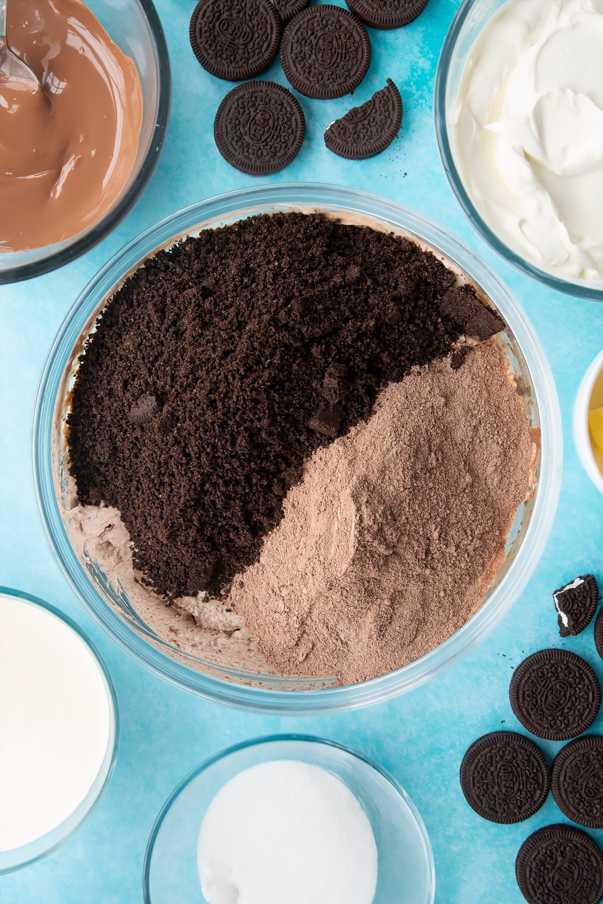 Overhead shot of whipped mixture, orea crumb and cocoa powder in a large clear bowl