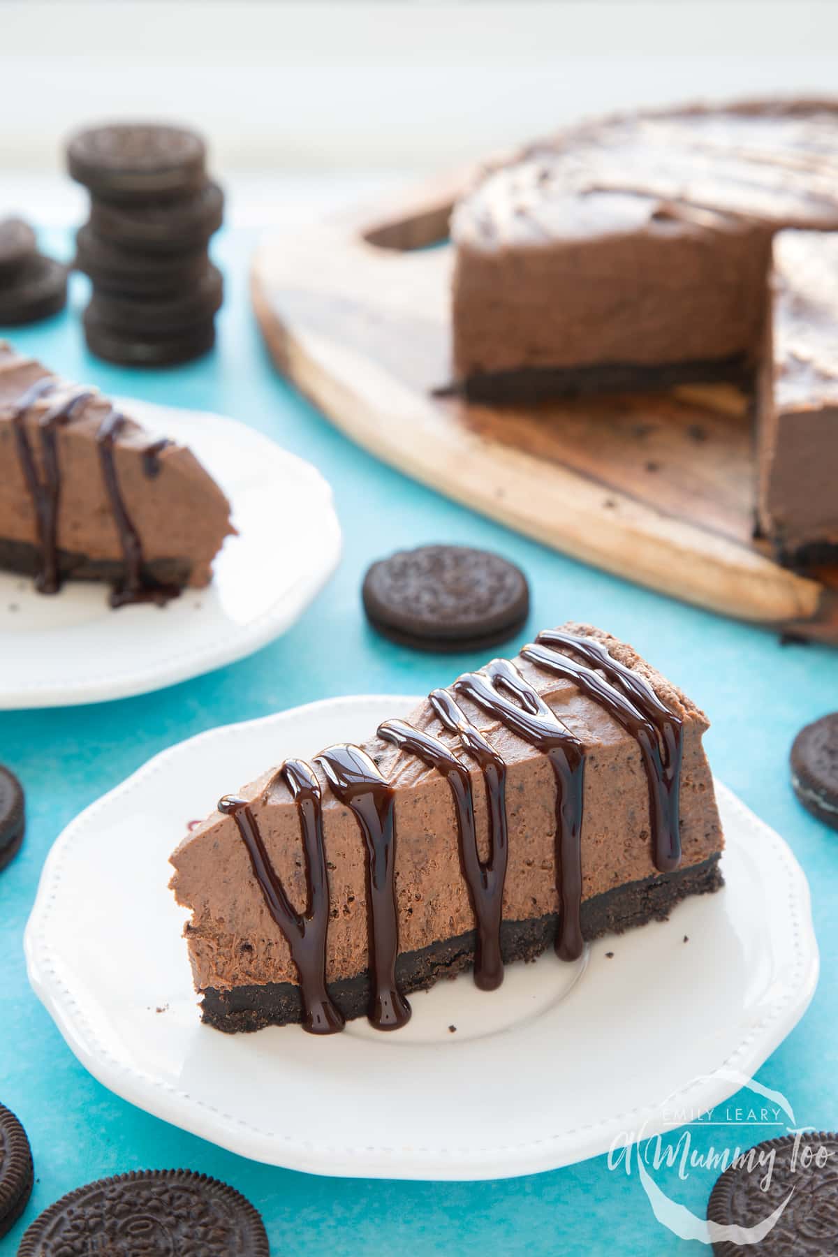 Front view shot of a piece of chocolate oreo cheesecake on a white plate drizzled with melted chocolate sauce