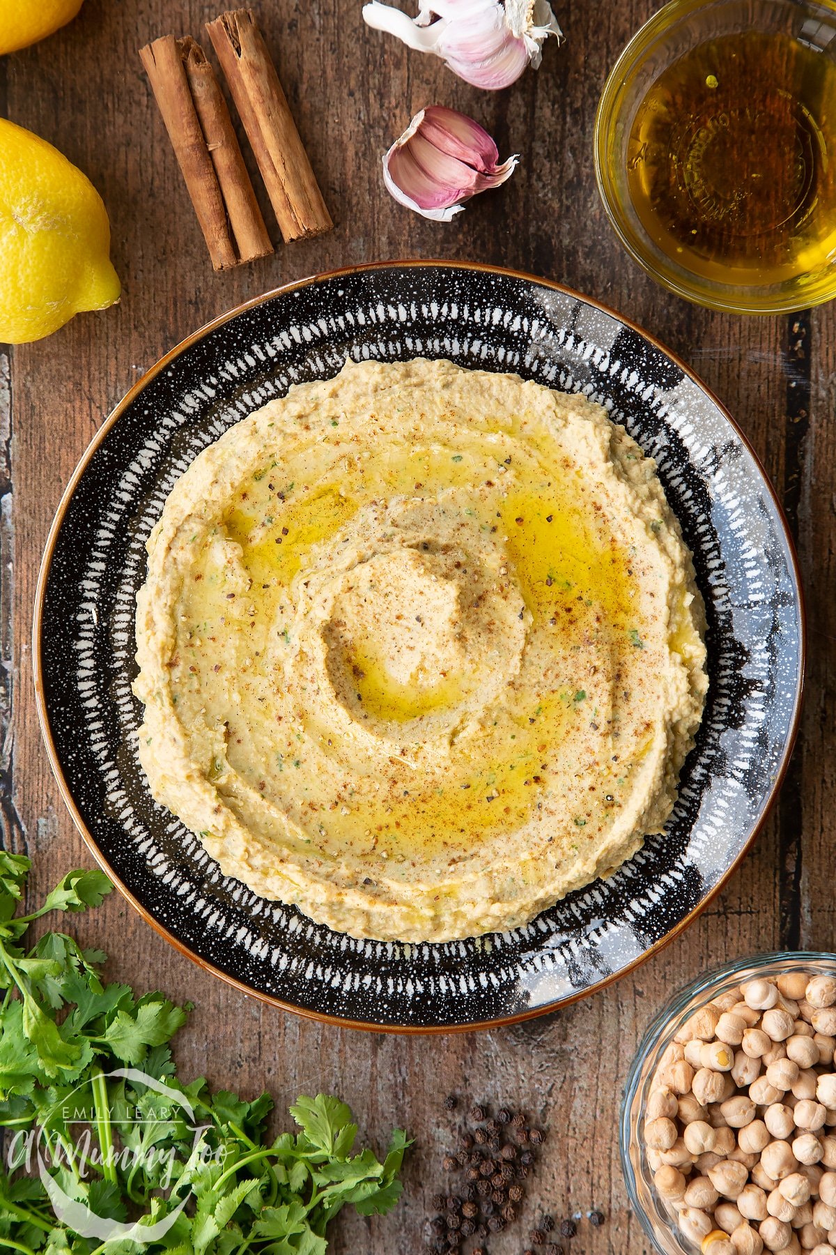 Cinnamon hummus served in a black and white bowl, shown from above. It has been seasoned with cinnamon and olive oil