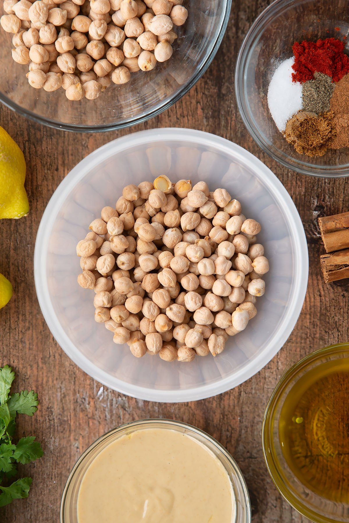 Dried chickpeas in a plastic bowl. Ingredients to make cinnamon hummus surround the bowl.