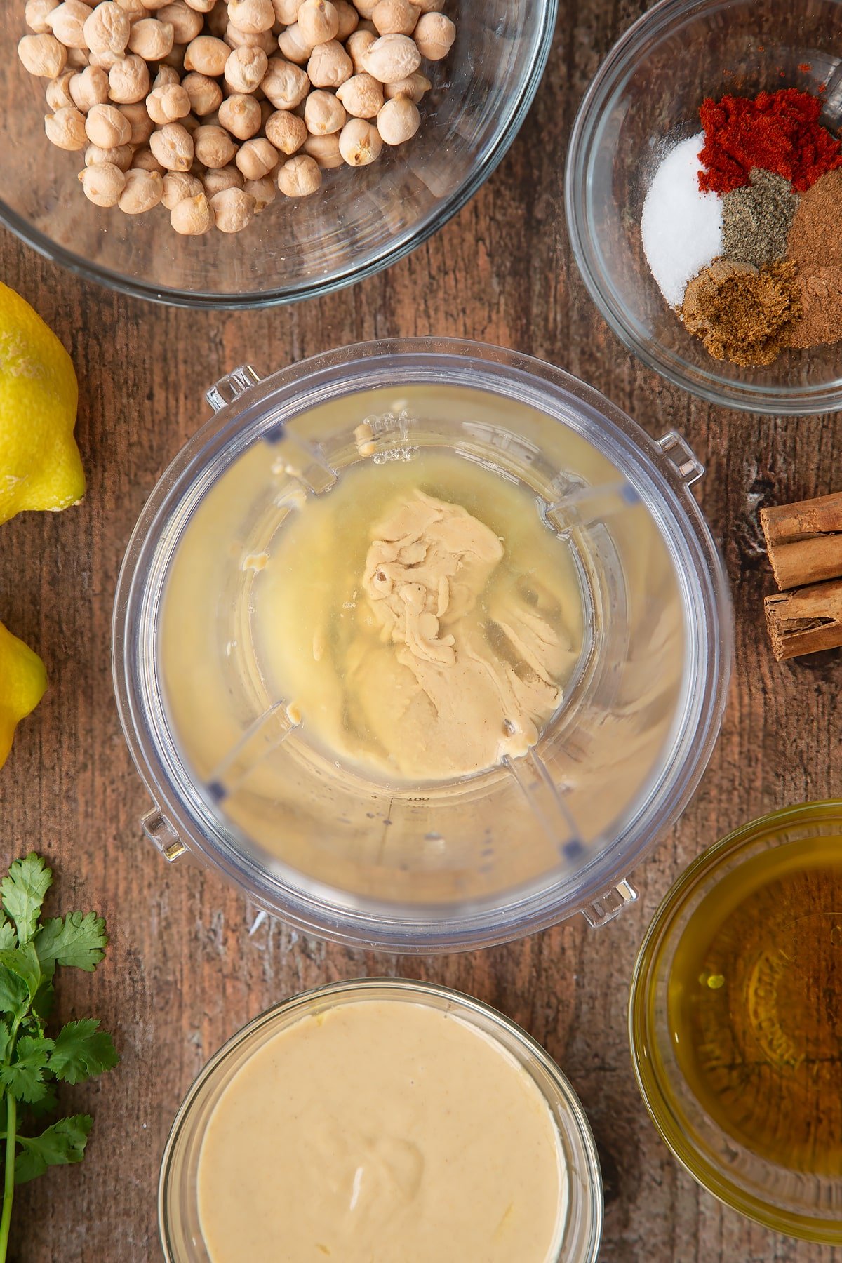 Tahini and lemon juice in a small blender bowl. Ingredients to make cinnamon hummus surround the bowl.