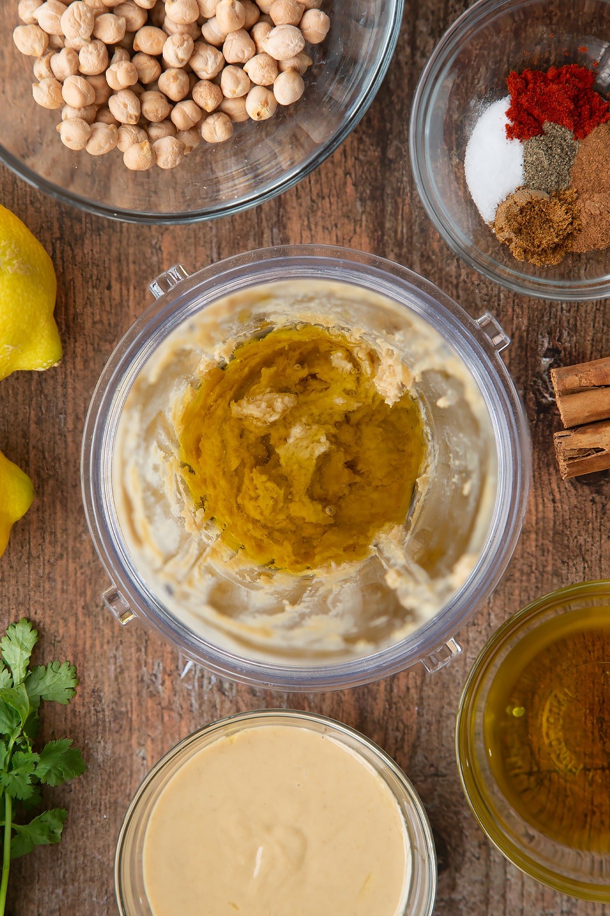 Tahini, lemon juice and oil in a small blender bowl. Ingredients to make cinnamon hummus surround the bowl.