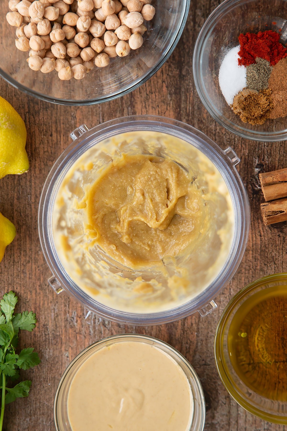 Tahini, lemon juice and oil whipped together in a small blender bowl. Ingredients to make cinnamon hummus surround the bowl.