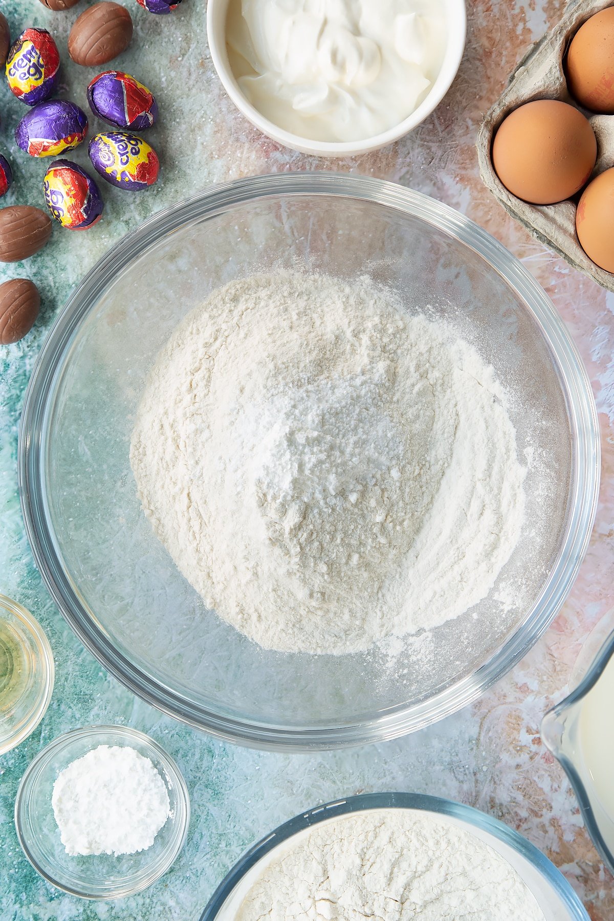 Self-raising flour and baking powder in a bowl. Ingredients to make Creme Egg pancakes surround the bowl.