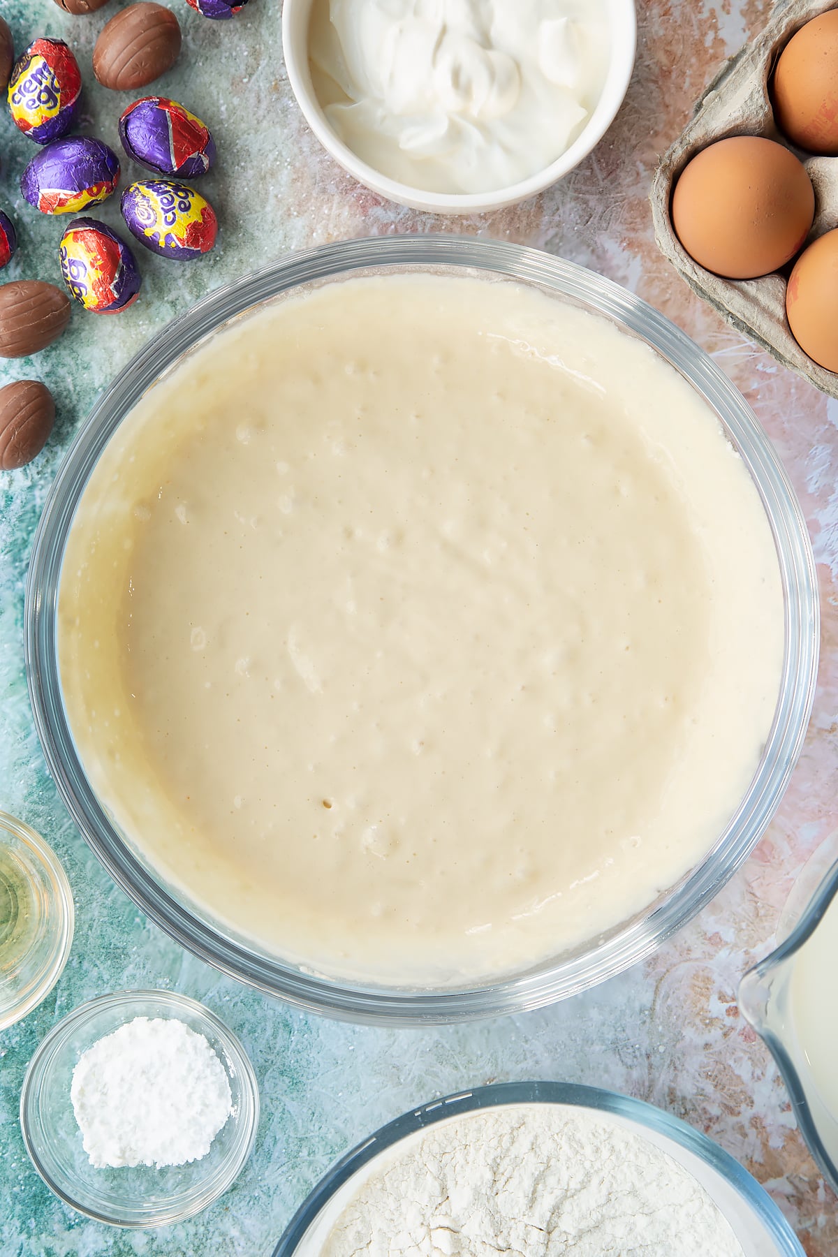 Pancake batter in a bowl. Ingredients to make Creme Egg pancakes surround the bowl.