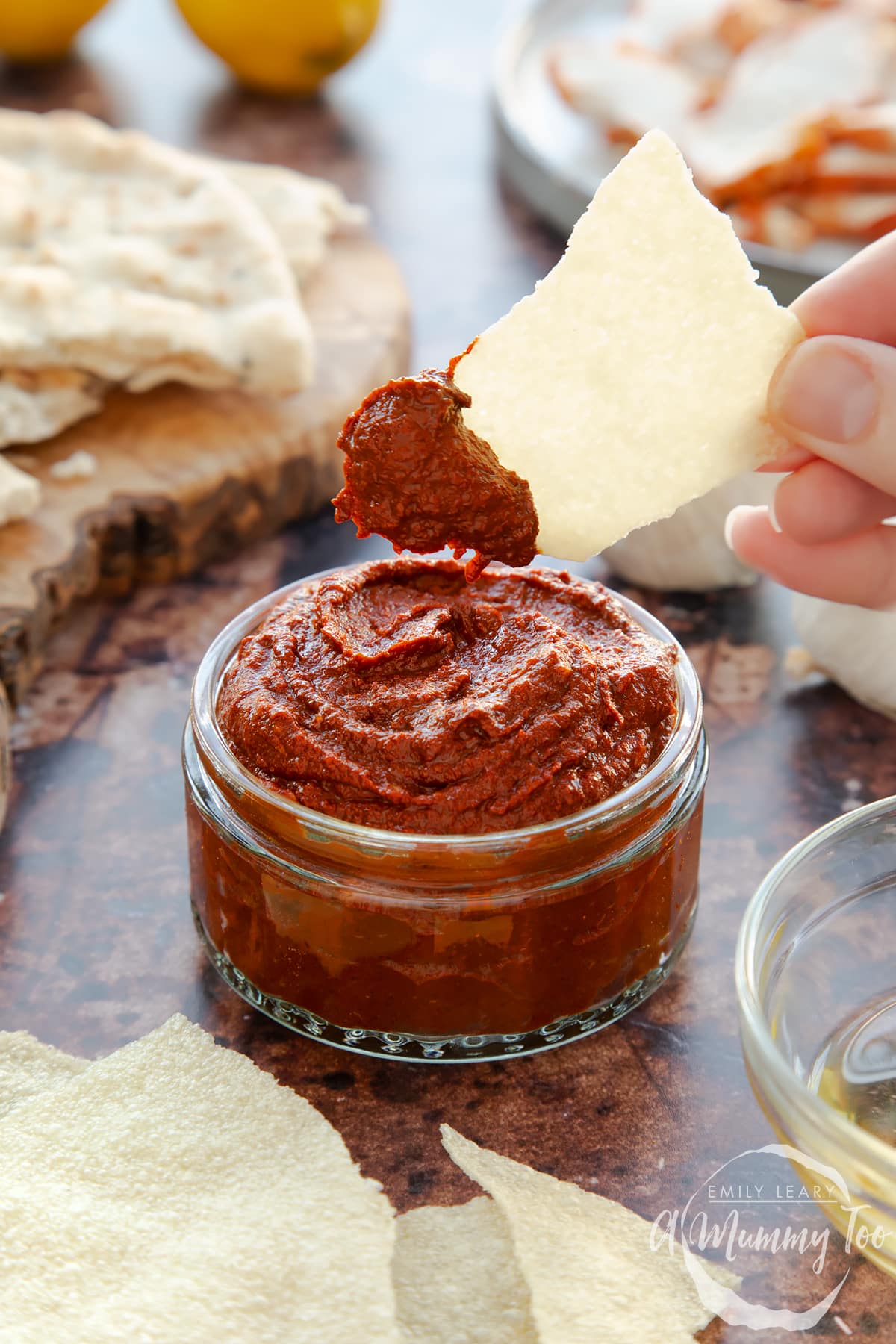 Front view of a hand holding a piece of bread dipping into garlic chutney in a small glass jar