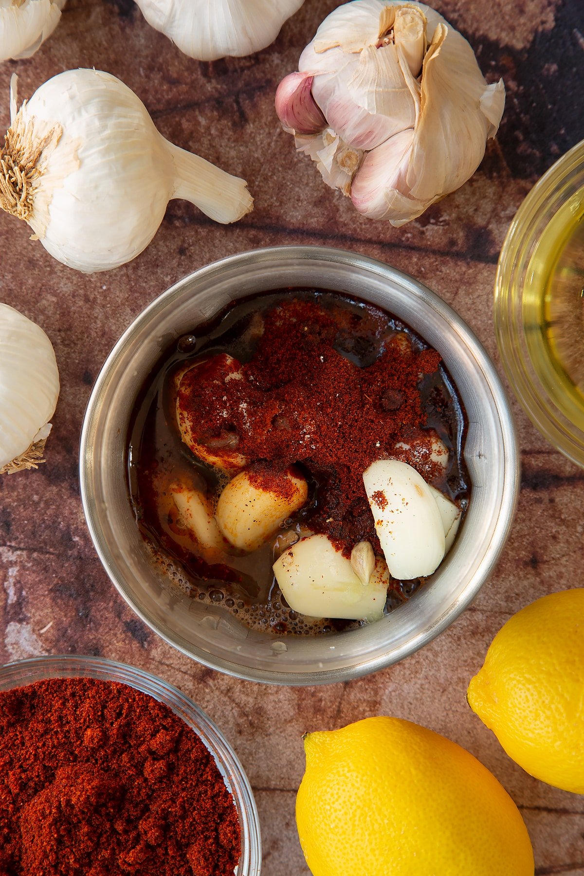 Overhead shot of garlic cloves, chilli powder, lemon juice, oil in a metal grinder