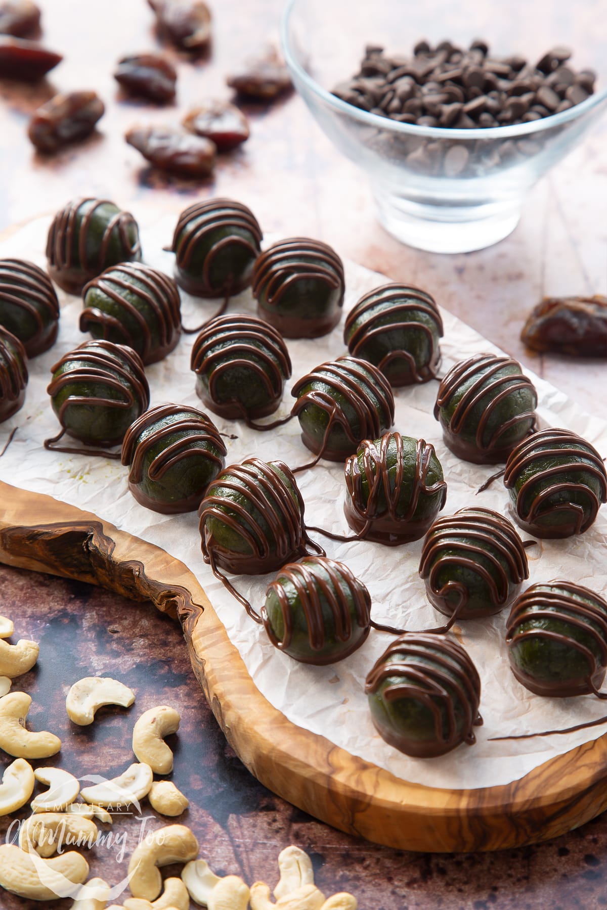 Matcha protein balls on a wooden board lined with baking paper. The balls are dark green and have been drizzled with dark chocolate.