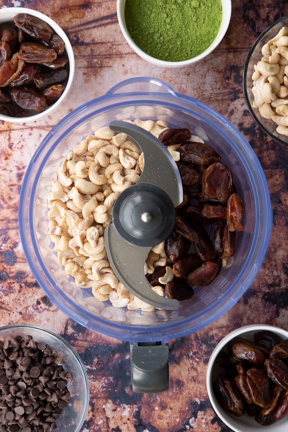 Dates and cashews in a blender bowl. Ingredients to make matcha protein balls surround the bowl.