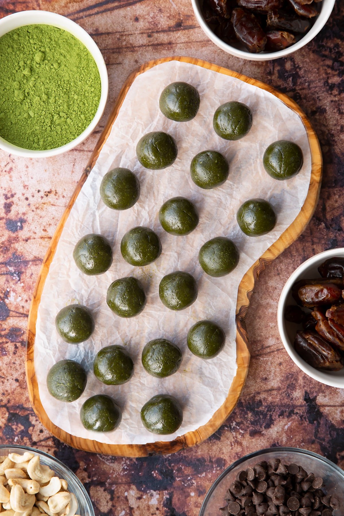 Matcha protein balls shown from above on a wooden board lined with baking paper. The balls are dark green.