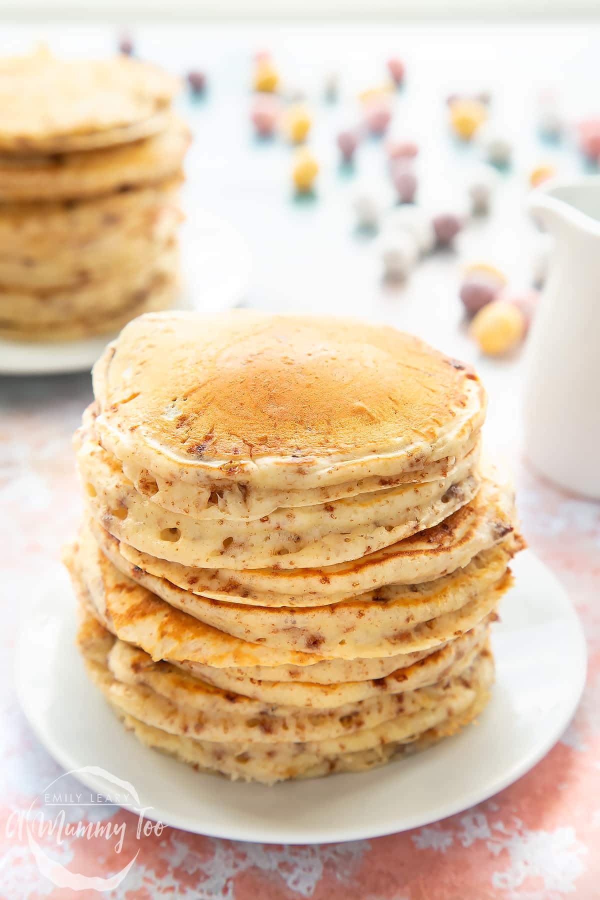 Thick, fluffy Mini Egg pancakes on a white plate in a tall stack. 