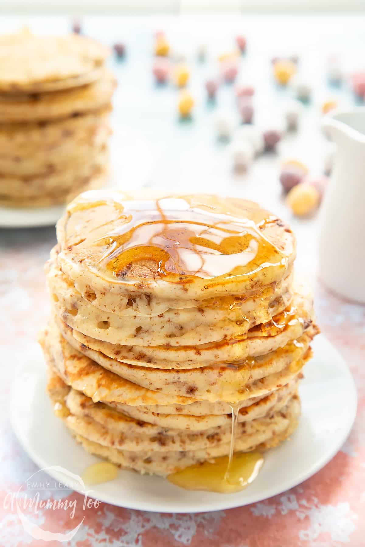 Thick, fluffy Mini Egg pancakes on a white plate in a tall stack. They are drizzled with syrup.