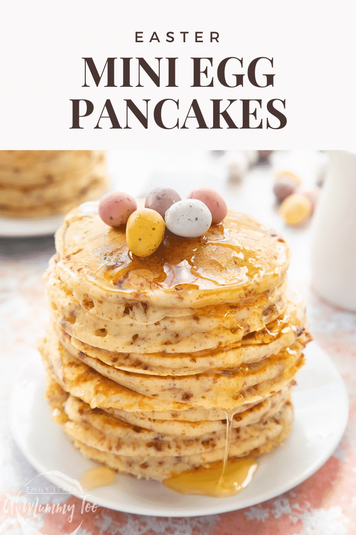 Tall, fluffy Mini Egg pancakes on a white plate in a tall stack. They are topped with syrup and Mini Eggs. Caption reads: Easter Mini Egg pancakes