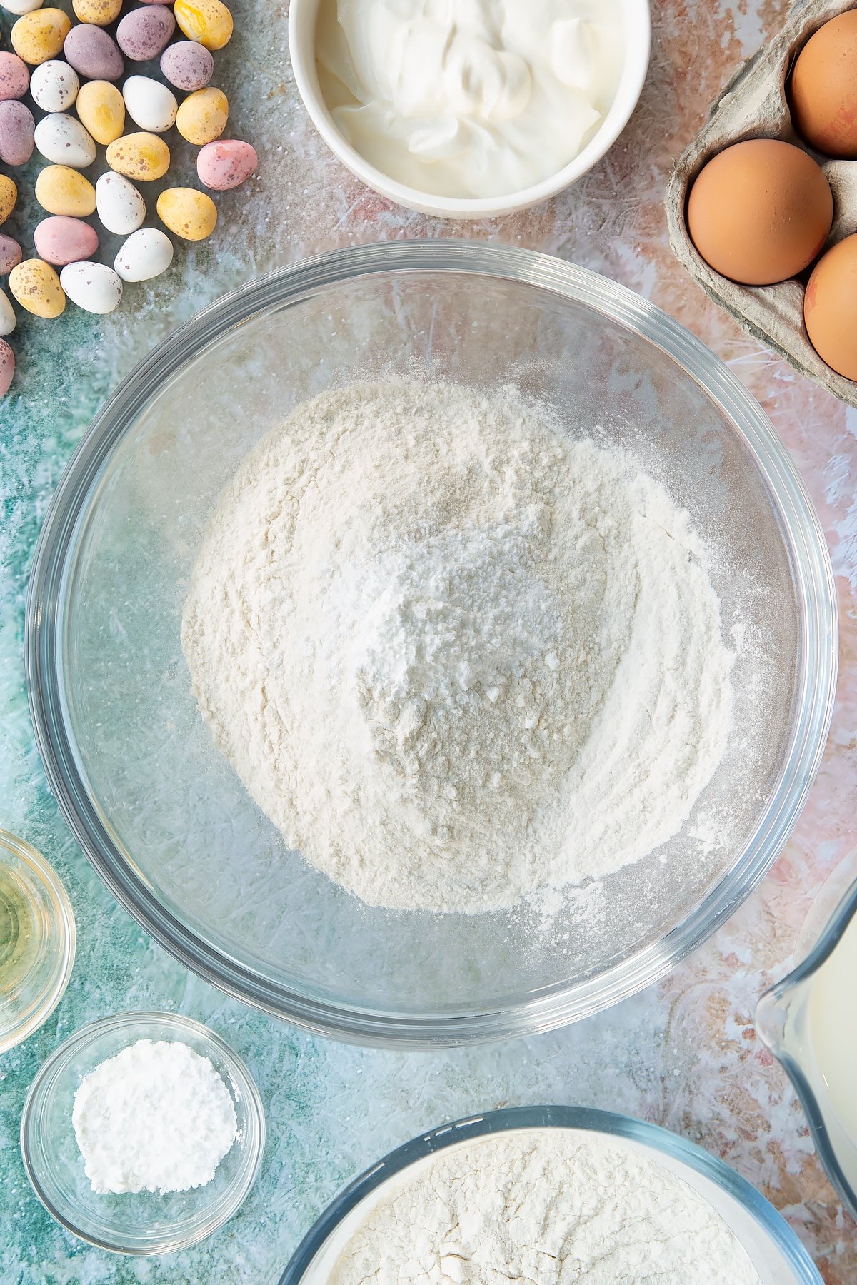 Flour and baking powder in a bowl. Ingredients to make Mini Egg pancakes surround the bowl.