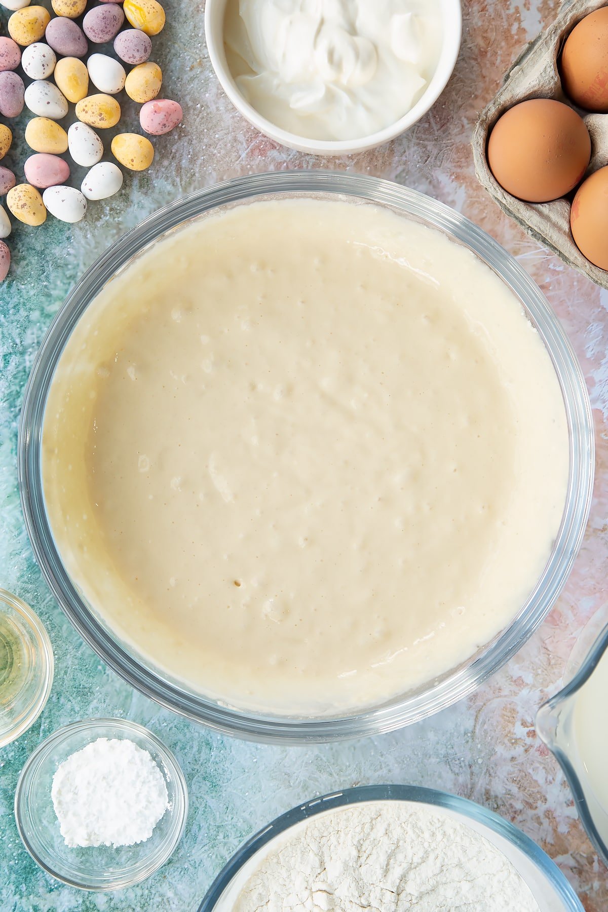 Pancake batter in a bowl. Ingredients to make Mini Egg pancakes surround the bowl.