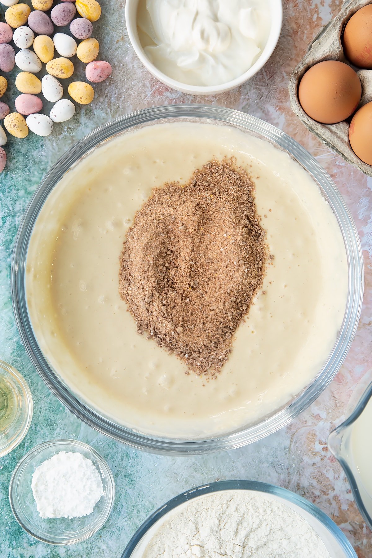 Pancake batter in a bowl with crushed Mini Eggs on top. Ingredients to make Mini Egg pancakes surround the bowl.