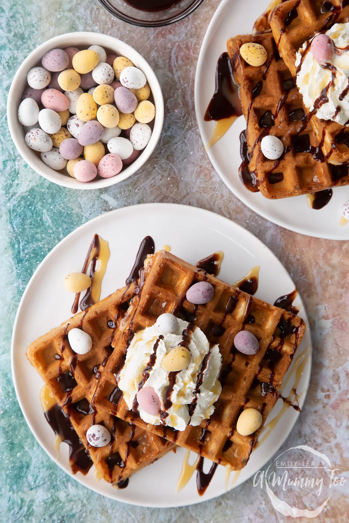 Mini egg waffles shown from above on white plates. They are topped with squirty cream, chocolate sauce, toffee sauce and Mini Eggs.