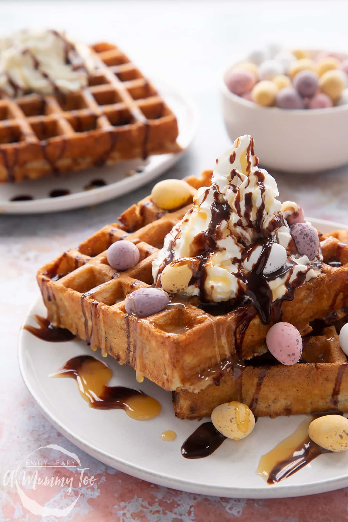 Mini egg waffles on a white plate. They are topped with squirty cream, chocolate sauce, toffee sauce and Mini Eggs.