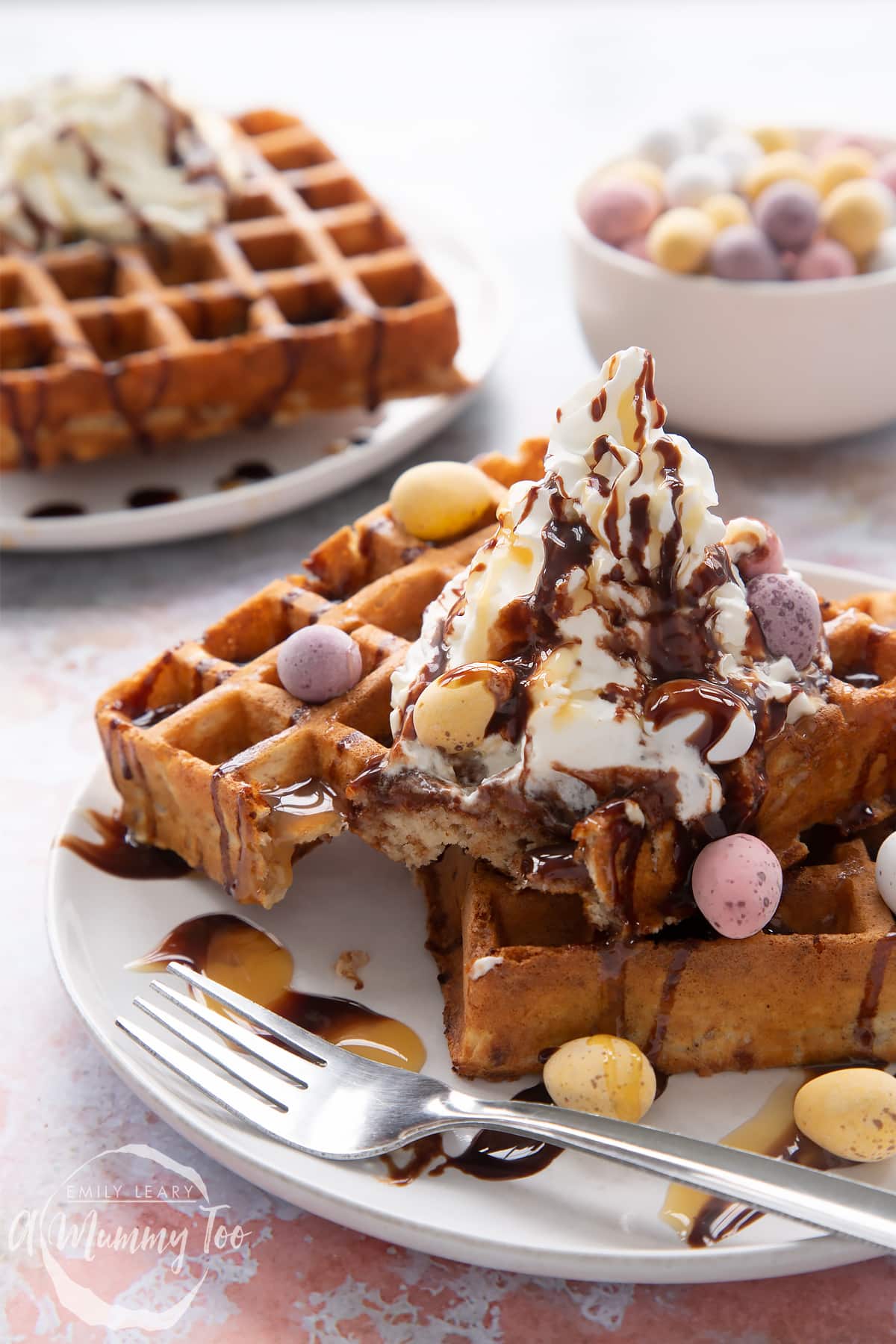 Mini egg waffles on a white plate with a fork. They are topped with squirty cream, chocolate sauce, toffee sauce and Mini Eggs.